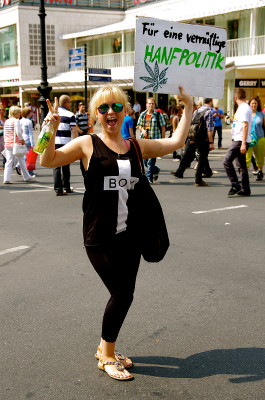 Foto einer lachenden Demoteilnehmerin mit einem Schild mit der Aufschrift 
